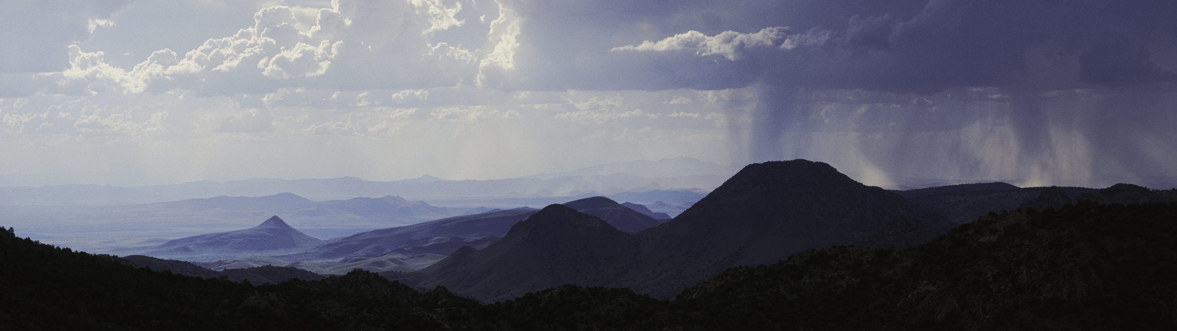 A summer storm drops rain over the Davis Mountains, with layered ridgelines fading into the distance