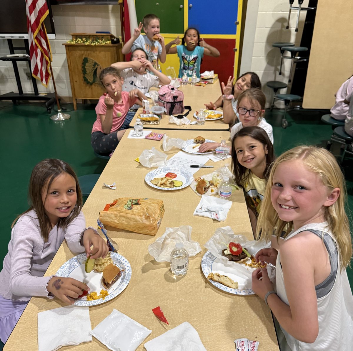 Elementary students enjoying burgers and waffle fries together at a cafeteria table