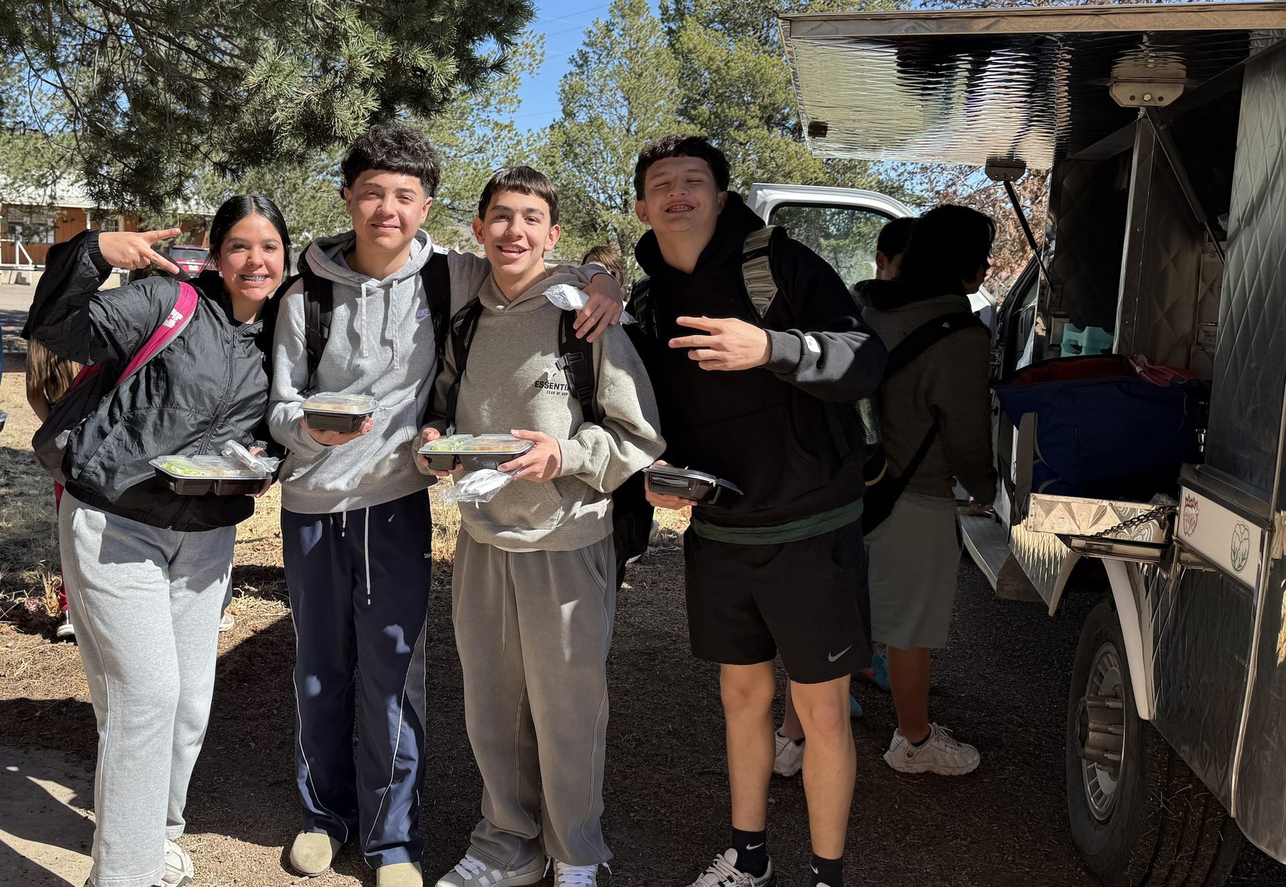 Four Fort Davis middle and high school students smiling with their lunch trays beside the serving trailer